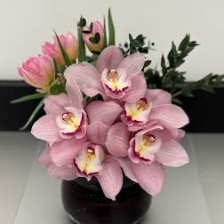 Pink orchids and tulips arranged in a dark glass vase