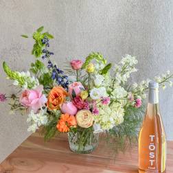 Mixed bouquet in a glass vase beside a bottle of rosé sparkling drink