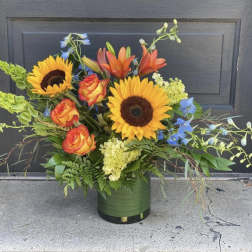Mixed bouquet with sunflowers, roses, lilies, and blue flowers in a green vase