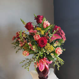 Mixed bouquet of red and pink flowers in a dark glass vase with a plaid ribbon.
