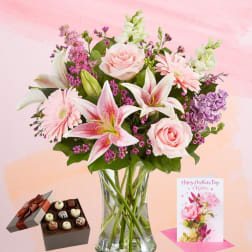 Pink and white mixed bouquet in a glass vase with chocolates and a greeting card