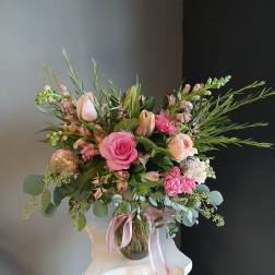 Pink and blush floral arrangement in a glass vase with a pink ribbon
