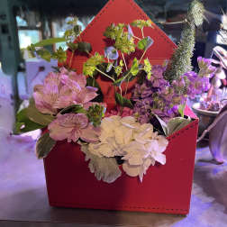 Pink and white flowers arranged in a red envelope-shaped box