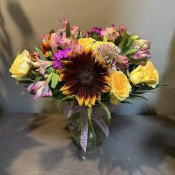 Mixed bouquet with a large dark sunflower and yellow roses in a glass vase