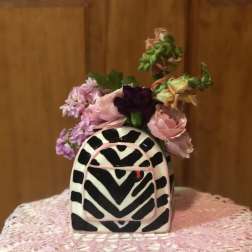 Small pink and purple flower arrangement in a black-and-white patterned vase