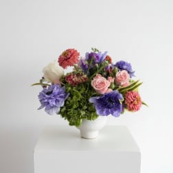 Mixed bouquet of pink, purple, and white flowers in a white vase