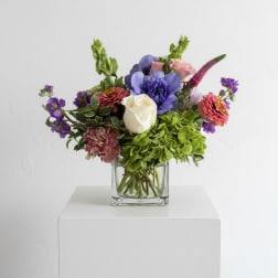 Mixed bouquet of purple, pink, white, and green flowers in a clear glass vase