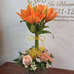 Orange lilies in a wooden box with peach roses and yellow pincushion blooms