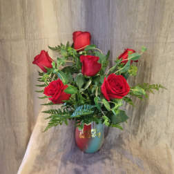 Red roses arranged in a multicolor vase with greenery