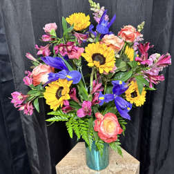 Mixed bouquet of sunflowers, roses, and purple iris in a blue vase