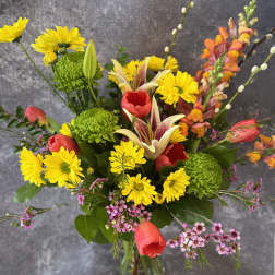 Mixed bouquet of yellow daisies, red tulips, and lilies in a glass vase