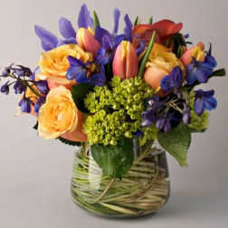 Mixed bouquet of orange roses, pink tulips, and purple flowers in a glass vase
