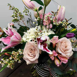 Bouquet of pink lilies, pale roses, and white filler flowers in a glass vase