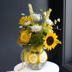 Sunflower and white flower arrangement in a glass vase with lemon slices