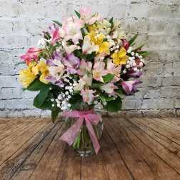 Mixed pink, yellow, and white flowers in a glass vase with a pink ribbon