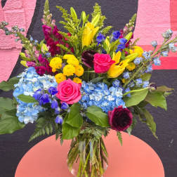 Colorful mixed bouquet with blue hydrangeas, yellow lilies, and pink roses in a clear glass vase.