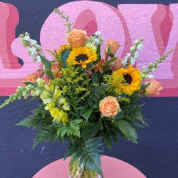 Mixed bouquet with sunflowers, peach roses, and yellow snapdragons in a glass vase
