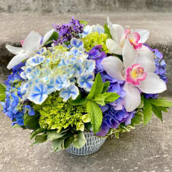 Bouquet of blue hydrangeas and white orchids in a patterned vase
