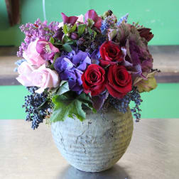 Mixed bouquet of roses, hydrangea, and purple blooms in a textured vase