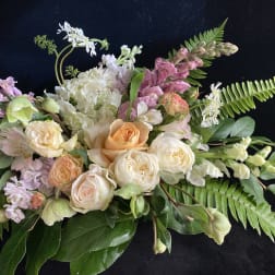 Pastel floral arrangement with roses, hydrangea, and snapdragons on a dark background