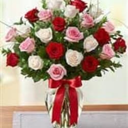 Bouquet of red, pink, and white roses in a glass vase with a red ribbon