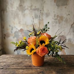 Orange roses and sunflowers arranged in a small terracotta pot