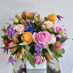 Mixed bouquet of pink, purple, orange, and cream flowers in a white vase