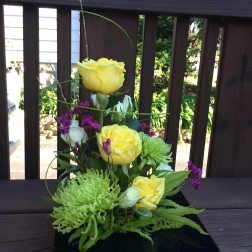 Yellow roses and green chrysanthemums in a black vase with purple accents