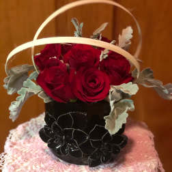 Basket arrangement of red roses with pale foliage in a black container