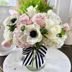 Pink and white bouquet in a glass vase with a striped ribbon
