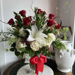 Red roses and white lilies arranged in a glass vase with a red ribbon