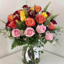 Mixed roses in pink, coral, yellow, and burgundy in a glass vase