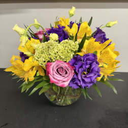 Mixed bouquet of pink, purple, and yellow flowers in a glass vase