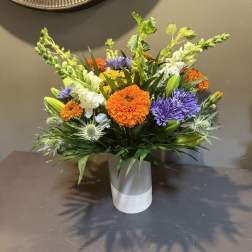 Bright mixed bouquet in a white vase with orange, purple, and white flowers