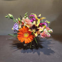 Mixed bouquet in a square glass vase with orange and yellow blooms