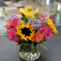 Bright mixed bouquet in a clear glass vase with sunflowers and pink roses