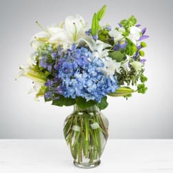 Blue hydrangeas and white lilies in a clear glass vase