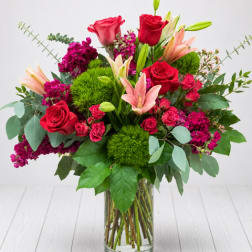 Bouquet of red roses, pink lilies, and purple flowers in a glass vase