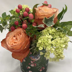 Peach roses with pink berries and pale green hydrangeas in a patterned vase