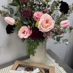 Mixed pink and burgundy bouquet in a tall vase with a box of macarons in front