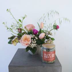 Pink rose bouquet in a vase beside a labeled glass jar candle