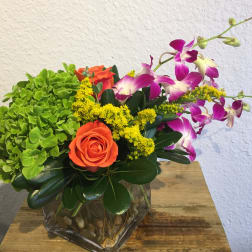 Orange rose and purple orchids in a glass vase with green hydrangea