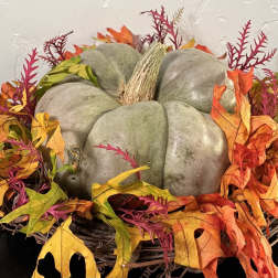 Decorative pumpkin centerpiece surrounded by autumn leaves in a wicker basket