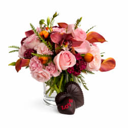 Pink and burgundy floral bouquet in a glass vase with chocolate hearts