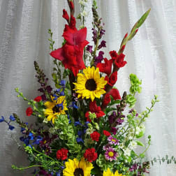 Tall mixed bouquet with sunflowers, red gladiolus, and blue flowers in a white vase