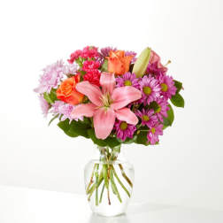 Pink lilies, roses, and purple daisies in a clear glass vase