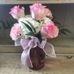 Pink roses and white hydrangeas in a purple glass vase with a pink ribbon
