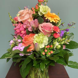 Mixed bouquet of pink, peach, yellow, and purple flowers in a glass vase