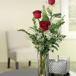Three red roses in a clear glass vase with white filler flowers