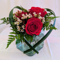 Red roses with small white blossoms in a glass vase